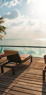 The image shows a serene poolside scene with sun loungers, umbrellas, palm trees, and a tranquil ocean view under a partly cloudy sky, ending the sentence.
