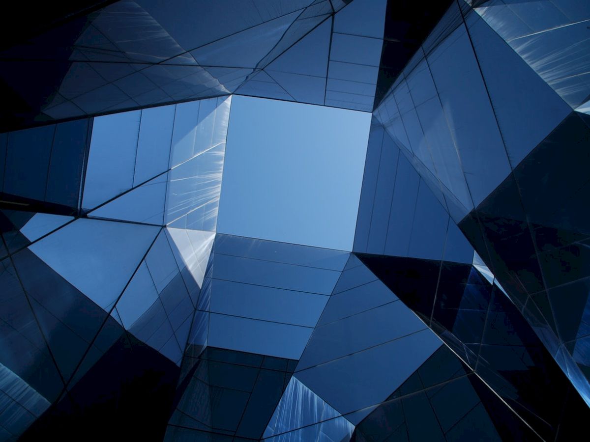 Looking up at a geometric structure made of reflective glass panels, forming an abstract view of the sky through angular shapes.