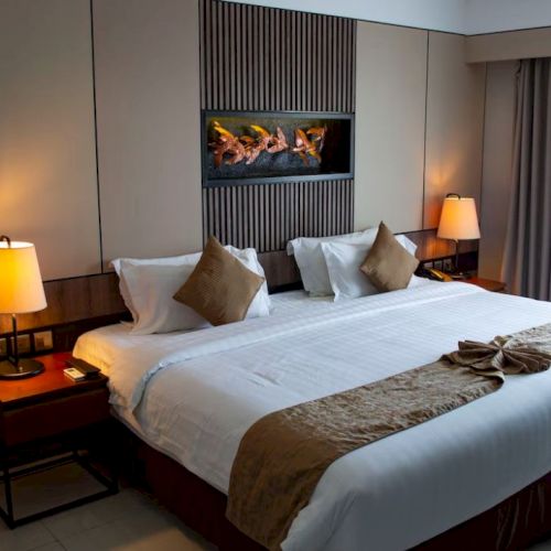 A well-lit hotel room with a large bed, two bedside tables with lamps, a wall decoration, and a window with curtains.