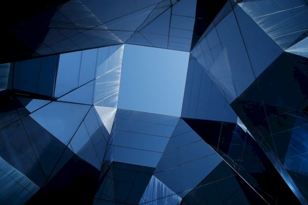 The image shows a geometric arrangement of reflective glass surfaces forming a skylight, with a clear view of the blue sky above.