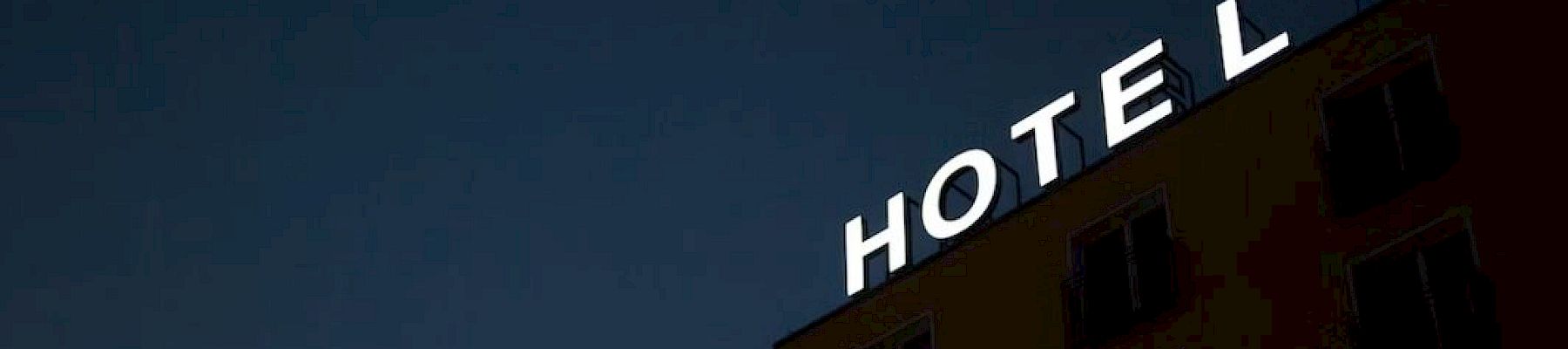 The image shows a building with a neon sign that reads "HOTEL," but the letter "T" is not illuminated, creating the word "HOEL".