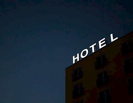 The image shows a building with a neon sign that reads "HOTEL," but the letter "T" is not illuminated, creating the word "HOEL".