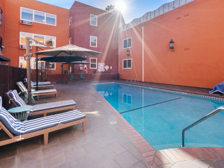 This image depicts a sunny outdoor pool area with lounge chairs and umbrellas next to an orange building.