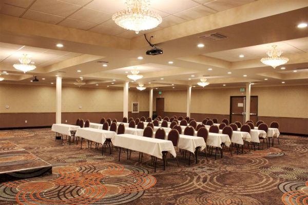 A conference room with chandeliers, tables covered in white cloths, and neatly arranged chairs, set up for a meeting or event, with carpet flooring.