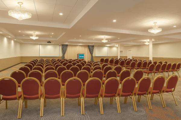The image shows an empty conference room with rows of red chairs and a small stage at the front, under soft, ambient lighting.
