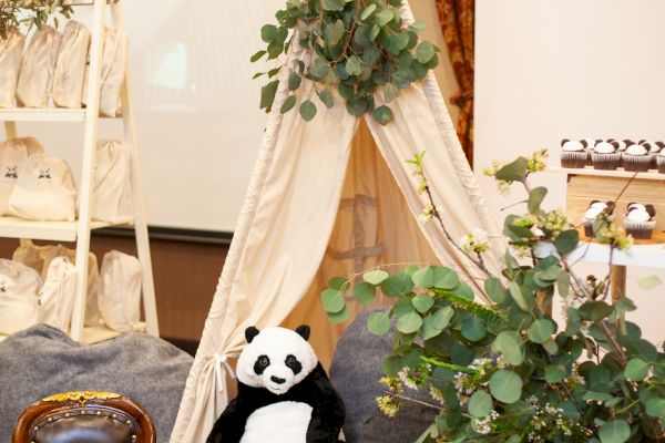 A cozy setup with a small tipi tent, a stuffed panda, a small chair, and various plants and greenery for decoration in an indoor room.