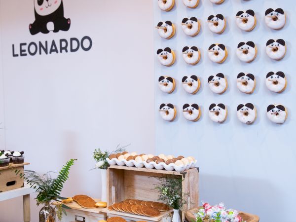 A decorated table with various pastries and a wall displaying panda-themed donuts. The wall has "Yummy in my tummy" written on it.