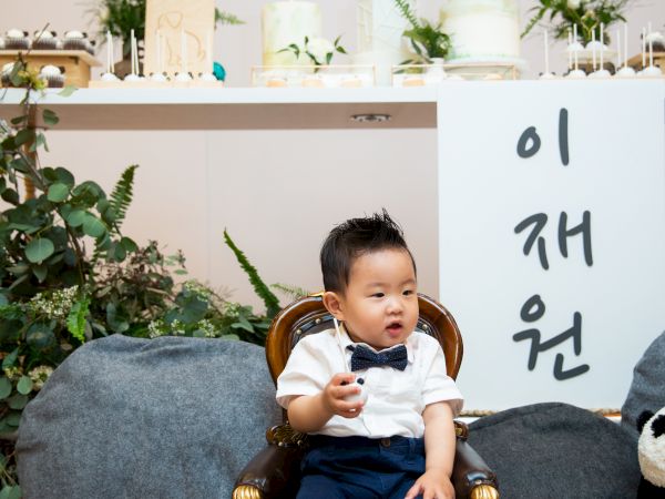 A child sits in a chair with a panda-themed backdrop. Korean text and the name "LEONARDO" are displayed above him, with plants and decor around.