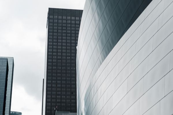 The image features modern architectural buildings, including a prominent curved structure with reflective metal panels against a cloudy sky.