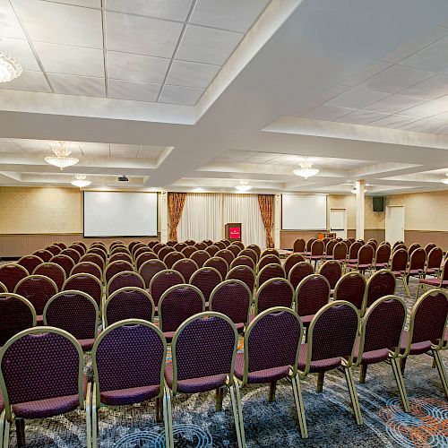 This is an image of an empty conference room setup with rows of chairs facing a projection screen, likely for a presentation or event.