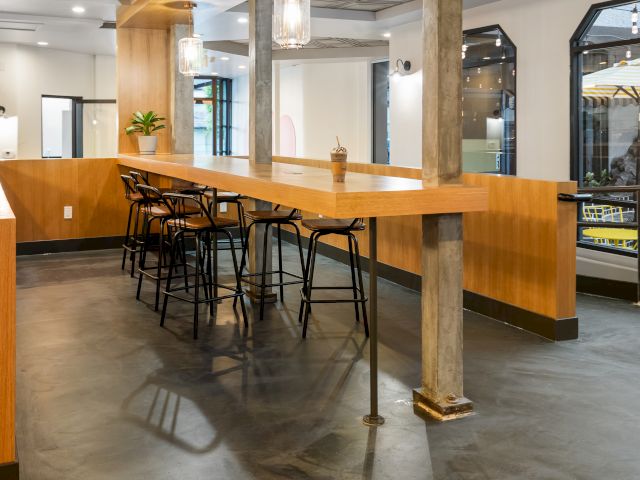 A modern hotel lobby bar with a wooden counter, black stools, and a potted plant.