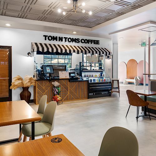 A modern coffee shop with wooden tables, chairs, and cozy booths. The counter features a sign that reads 