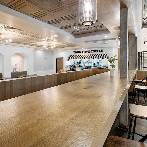 A modern coffee shop with a long wooden counter, chairs, and a sign reading 