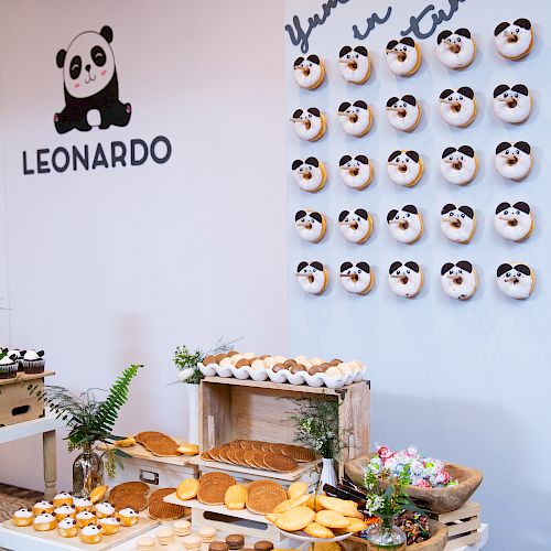 The image shows a decorated food station with panda-themed donuts on a wall that says “Yummy in my tummy” and other baked goods on tables.