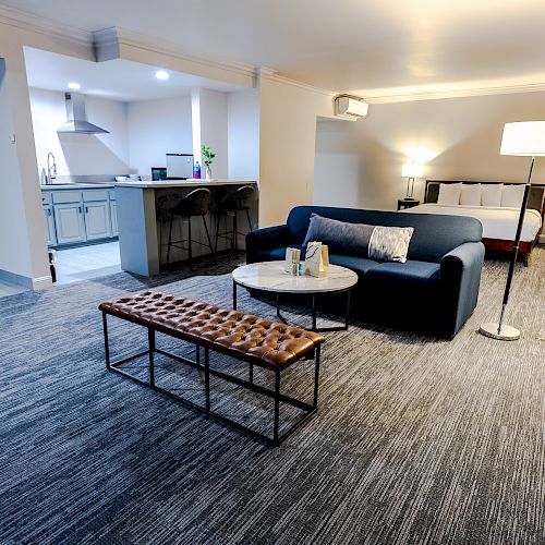 A modern, cozy living space with a sofa, coffee table, floor lamp, and a kitchen area in the background, featuring contemporary decor and lighting.