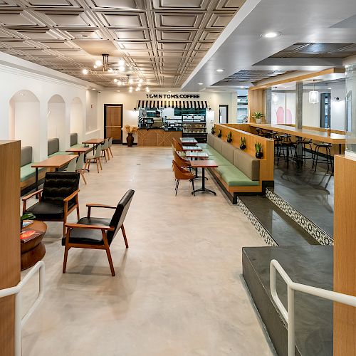 The image shows a modern coffee shop with wooden booths, tables, chairs, and a counter at the back, all under a decorative ceiling.