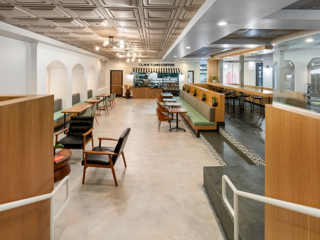 A wide view of a hotel lobby with seating areas, tables, booths, and a high ceiling.