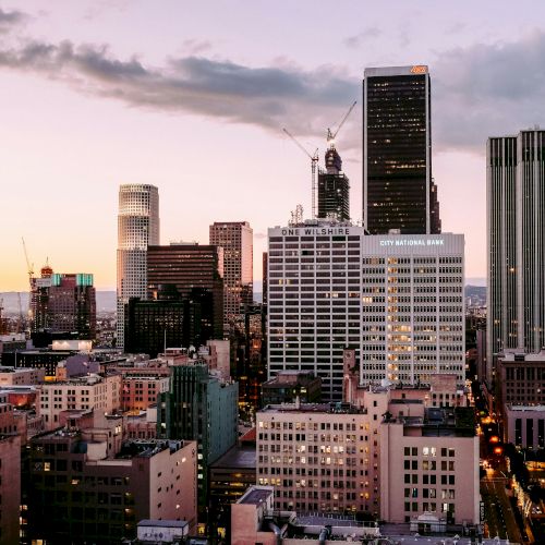 City skyline at dusk with buildings illuminated by the setting sun.