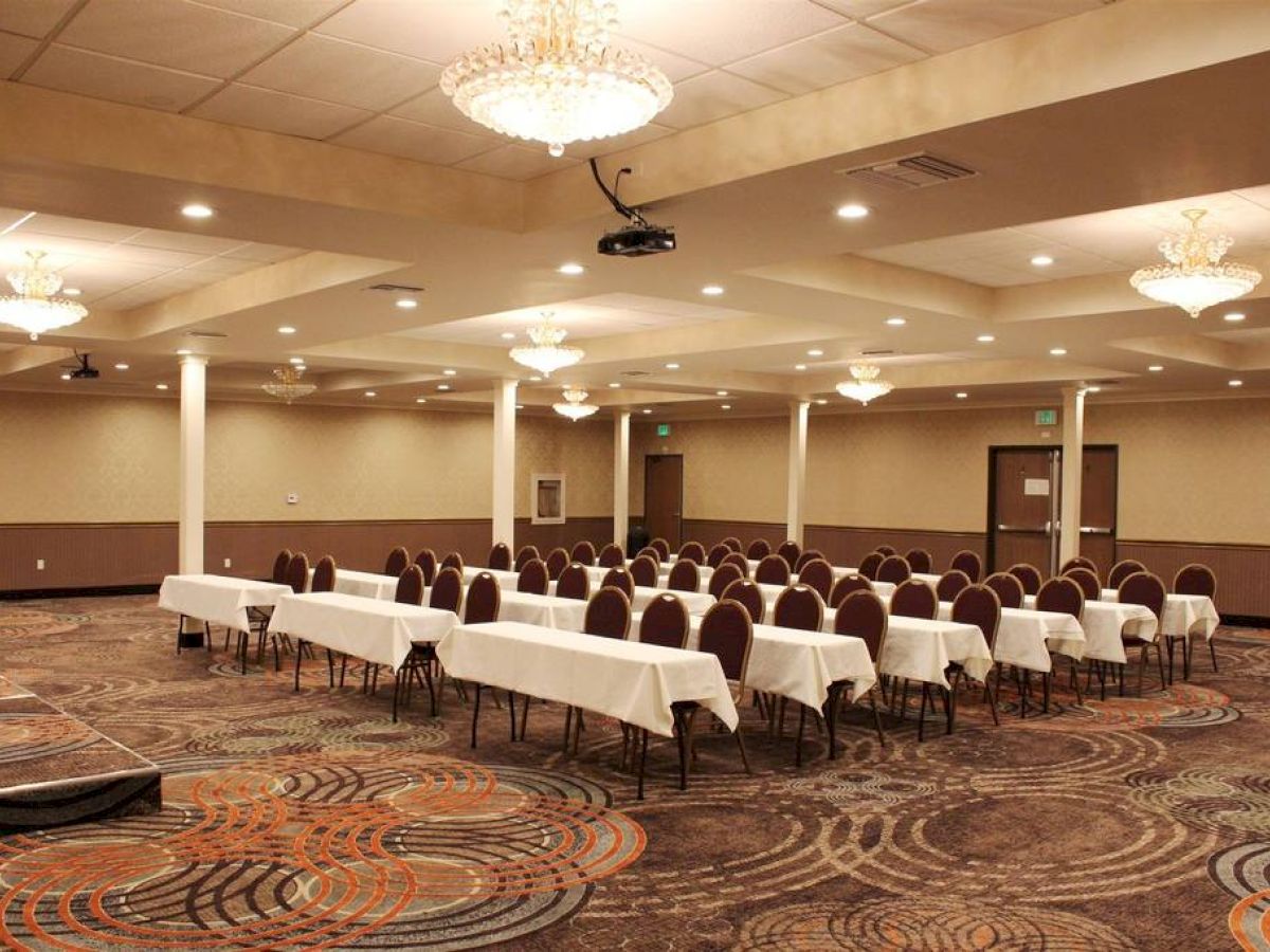 An empty conference room with rows of tables and chairs, chandeliers, and a patterned carpet, ready for a meeting or event.