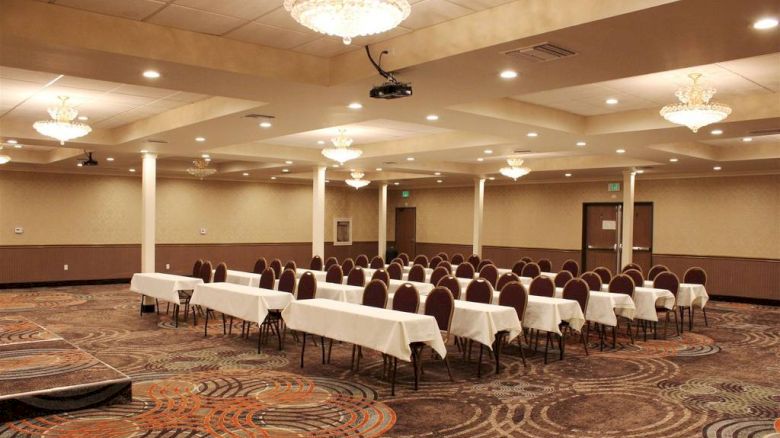 An empty conference room with rows of tables and chairs, chandeliers, and a patterned carpet, ready for a meeting or event.