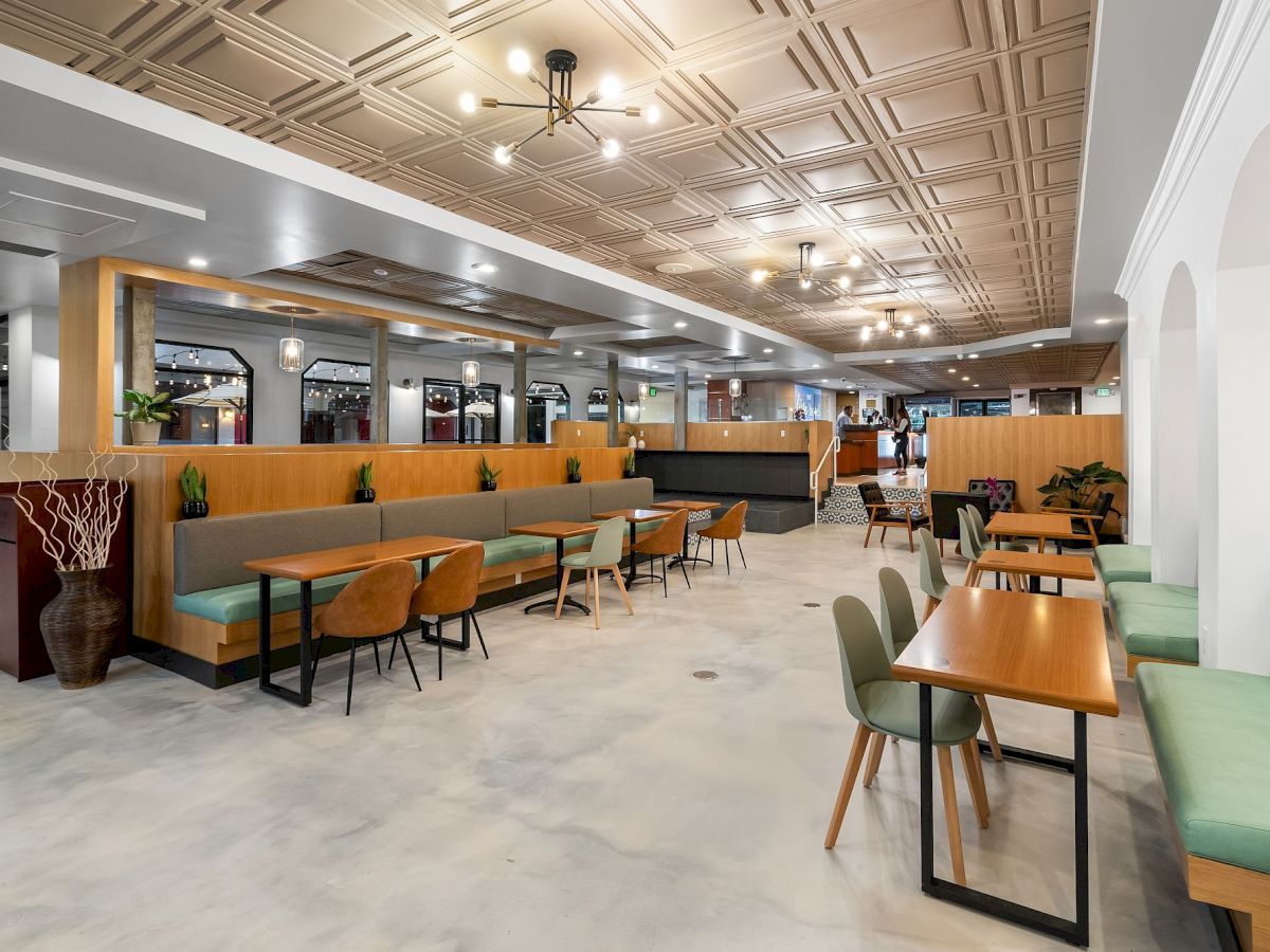 A modern, spacious dining area with wooden tables, green upholstered seating, and minimalist décor is depicted in this image.