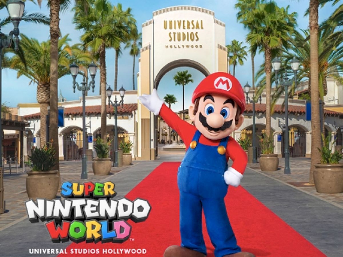 A character in blue overalls and a red cap stands on a red carpet in front of the Universal Studios Hollywood entrance.