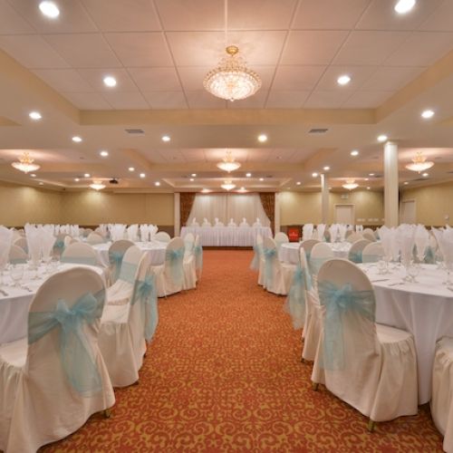 It’s a decorated banquet hall with round tables, white chair covers, light blue ribbons, and crystal chandeliers. It looks ready for an event.