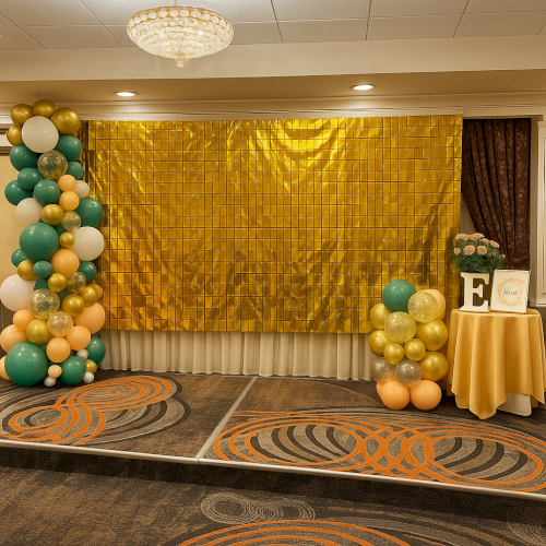 A decorated venue with a gold backdrop, colorful balloon arrangements, flowers, and a table with a frame and a letter "E".