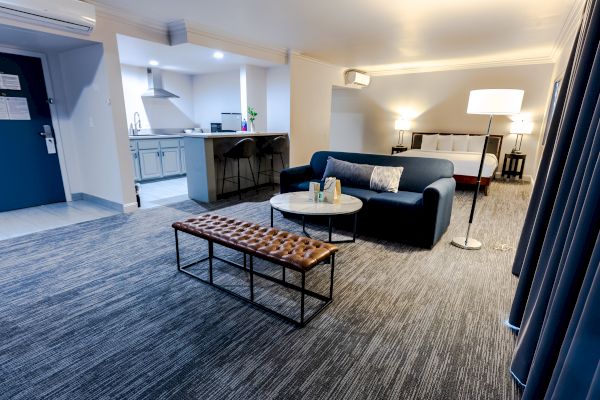 A modern living room with a sofa, coffee table, floor lamp, and bench. Open kitchen in the background; carpeted floor. End of sentence.