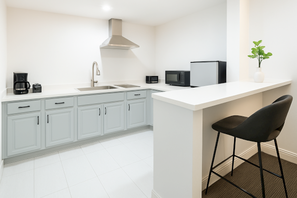 A modern kitchen with light cabinets, coffee maker, toaster, sink, microwave, mini-fridge, and bar stool.