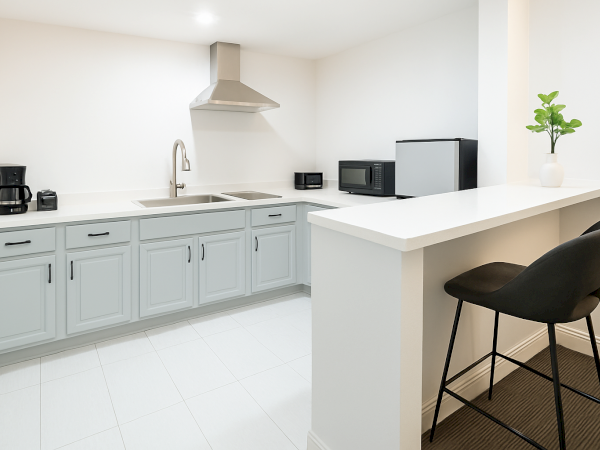 A modern kitchen with light cabinets, coffee maker, toaster, sink, microwave, mini-fridge, and bar stool.