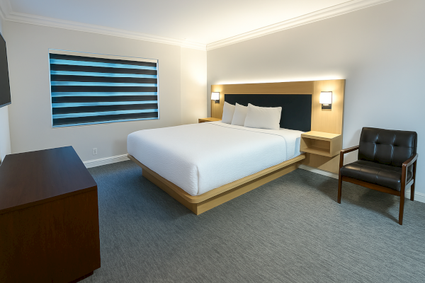 A modern hotel room with a large bed, stylish armchair, window with blinds, and sleek minimalistic furniture for a cozy stay.