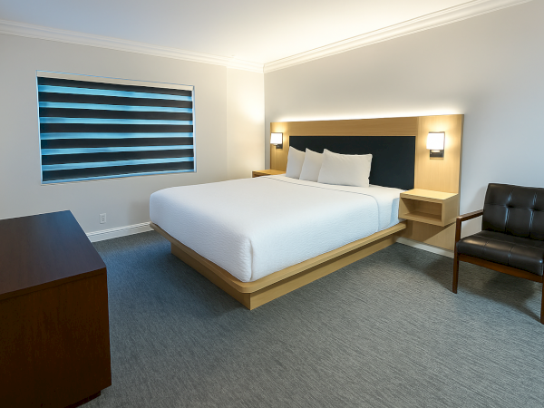 A modern hotel room with a large bed, stylish armchair, window with blinds, and sleek minimalistic furniture for a cozy stay.