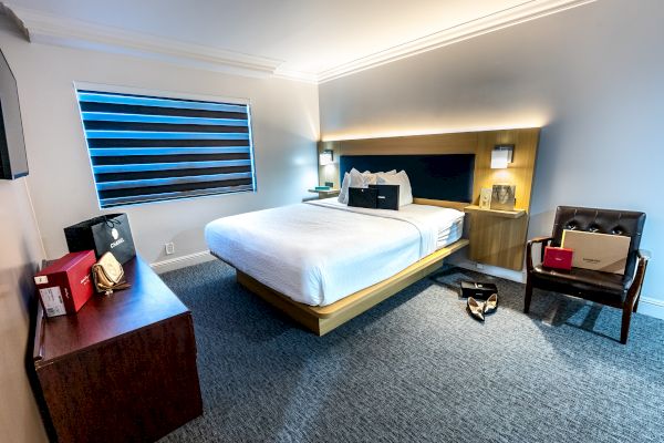 A modern hotel room with a neatly made bed, shopping bags, laptop, and shoes scattered on the floor, sleek furniture, and striped blinds ends the sentence.