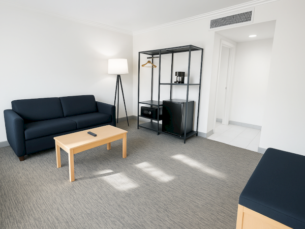 A modern living space with a blue sofa, lamp, coffee table, shelving, and a small fridge, in a minimalist style.