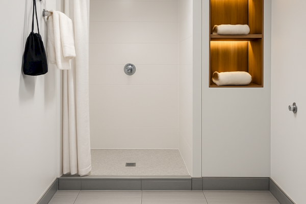 Modern bathroom with a shower, white curtain, towel shelf, and light gray floor tiles, creating a clean and minimalist appearance.