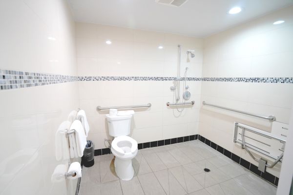 This image shows a spacious, accessible restroom with a toilet, grab bars, a shower area, and folded towels on the wall.