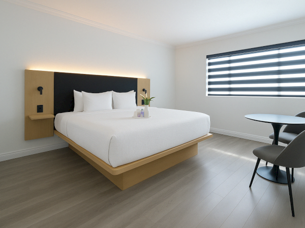 A modern bedroom with a minimalist design features a large bed, a table with two chairs, and a window with striped blinds.