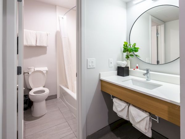 The image shows a modern bathroom with a sink, mirror, and a separate area with a toilet and bathtub.