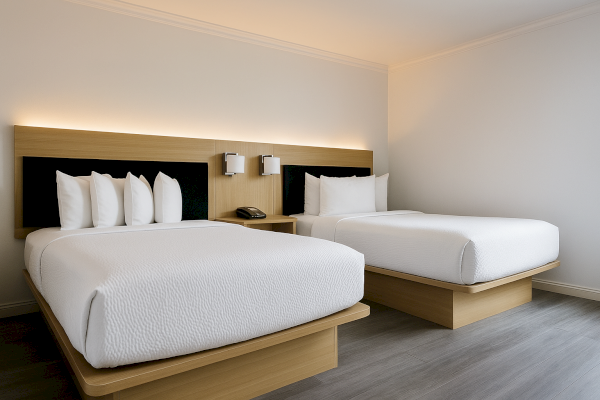 Two neatly made single beds with white linens in a modern hotel room, featuring a wooden headboard and wall lamps.