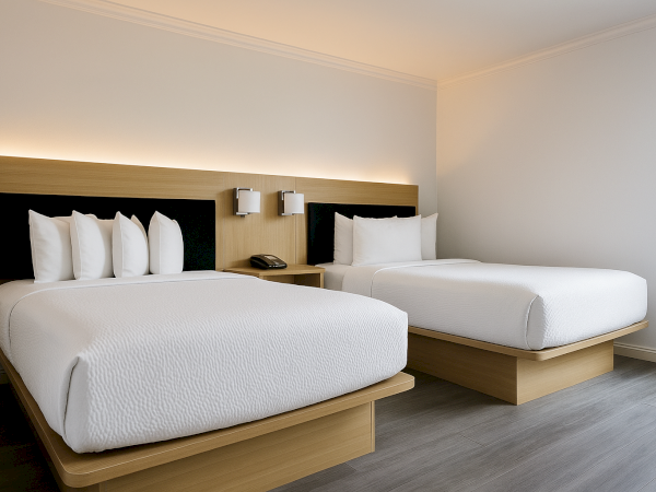 Two neatly made single beds with white linens in a modern hotel room, featuring a wooden headboard and wall lamps.