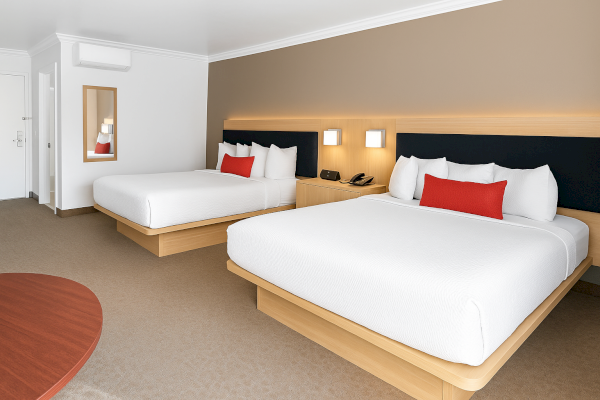 The image shows a hotel room with two beds, a bedside table with lamps, a phone, and a mirror on the wall.
