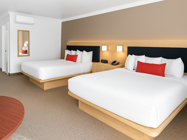 The image shows a hotel room with two beds, a bedside table with lamps, a phone, and a mirror on the wall.