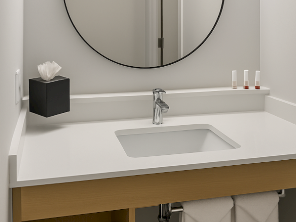A minimalist bathroom with a round mirror, sink, tissue box, toiletries, and towels under the counter in a wooden shelf.