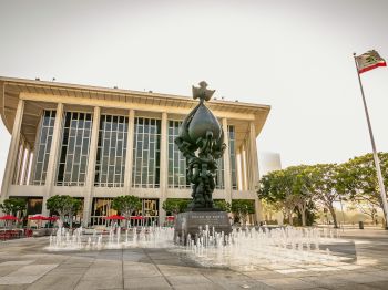 A building with tall columns, a statue titled "Peace on Earth," a fountain, and the California state flag in the background.