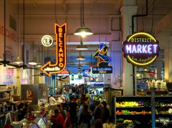 A bustling indoor market with neon signs, various stalls, and many people shopping and dining in Los Angeles.
