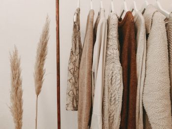 Clothing items on hangers in neutral tones beside pampas grass in a minimalistic setting.
