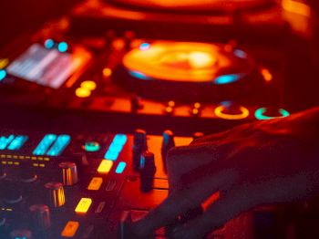 A DJ setup with glowing lights and a hand adjusting controls, surrounded by an orange and blue ambient lighting.
