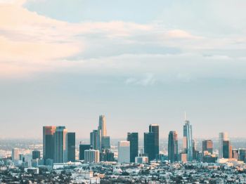 A cityscape with tall skyscrapers under a sky with scattered clouds, showcasing an urban skyline during sunrise or sunset.