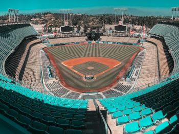 The image shows an empty baseball stadium with neatly mowed grass, teal seats, and large scoreboards behind the outfield.